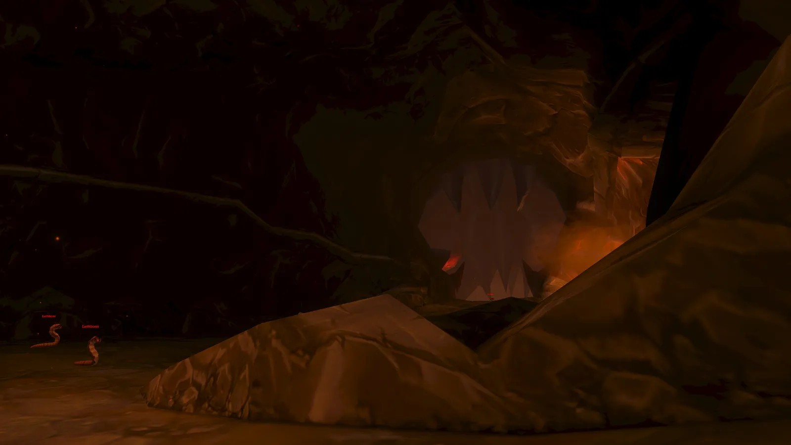The toothed, maw-like entrance tunnel of Ragefire Chasm glowing orange in the dark, with two Earthborers on the cave floor on the left